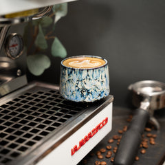 Cappuccino Tasse auf einer Siebträgermaschine mit Latte Art darin.