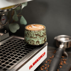 Cappuccino Tasse auf einer Siebträgermaschine mit Latte Art darin.