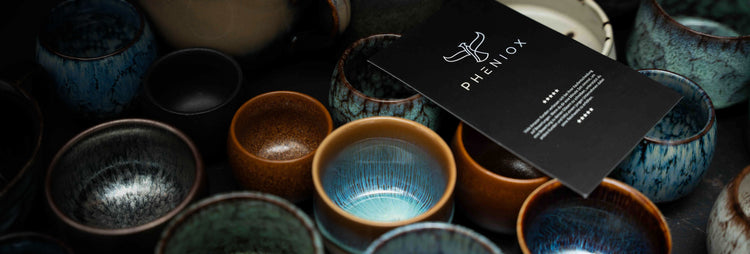 Viele Bunte PHENIOX Steinguttassen stehen nebeneinander. Auf ihnen liegt ein PHENIOX Flyer.